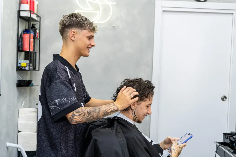 Adri, de perfil y sonriendo, charlando con el cliente mientras le mira el pelo
