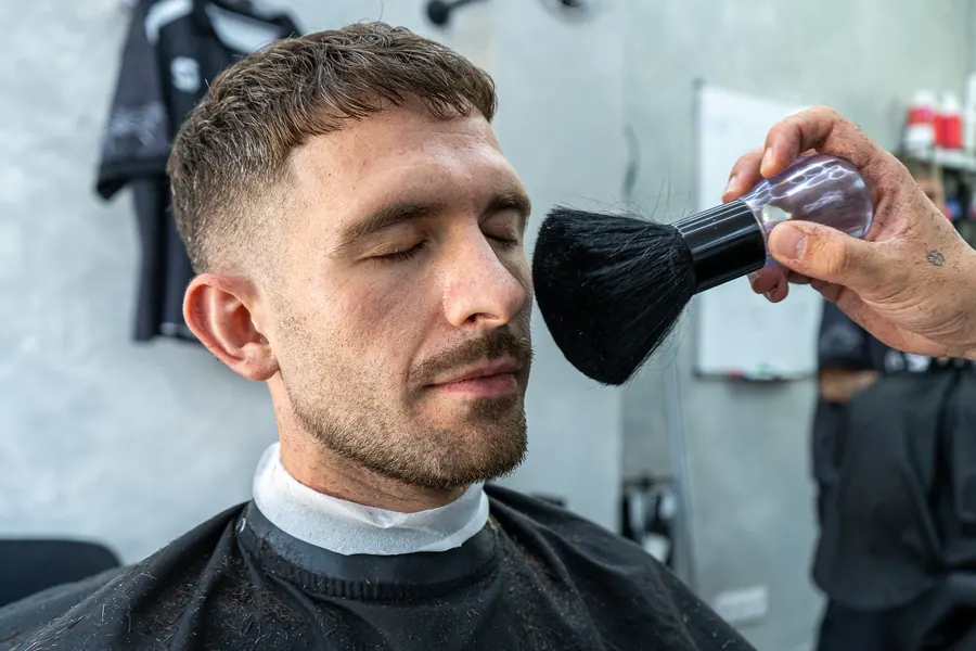 Cliente con los ojos cerrados mientras le retiran el pelo de la cara con el plumero